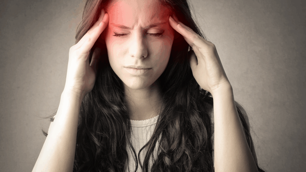 "Woman experiencing a tension headache caused by desk job stress, pressing her temples with visible discomfort